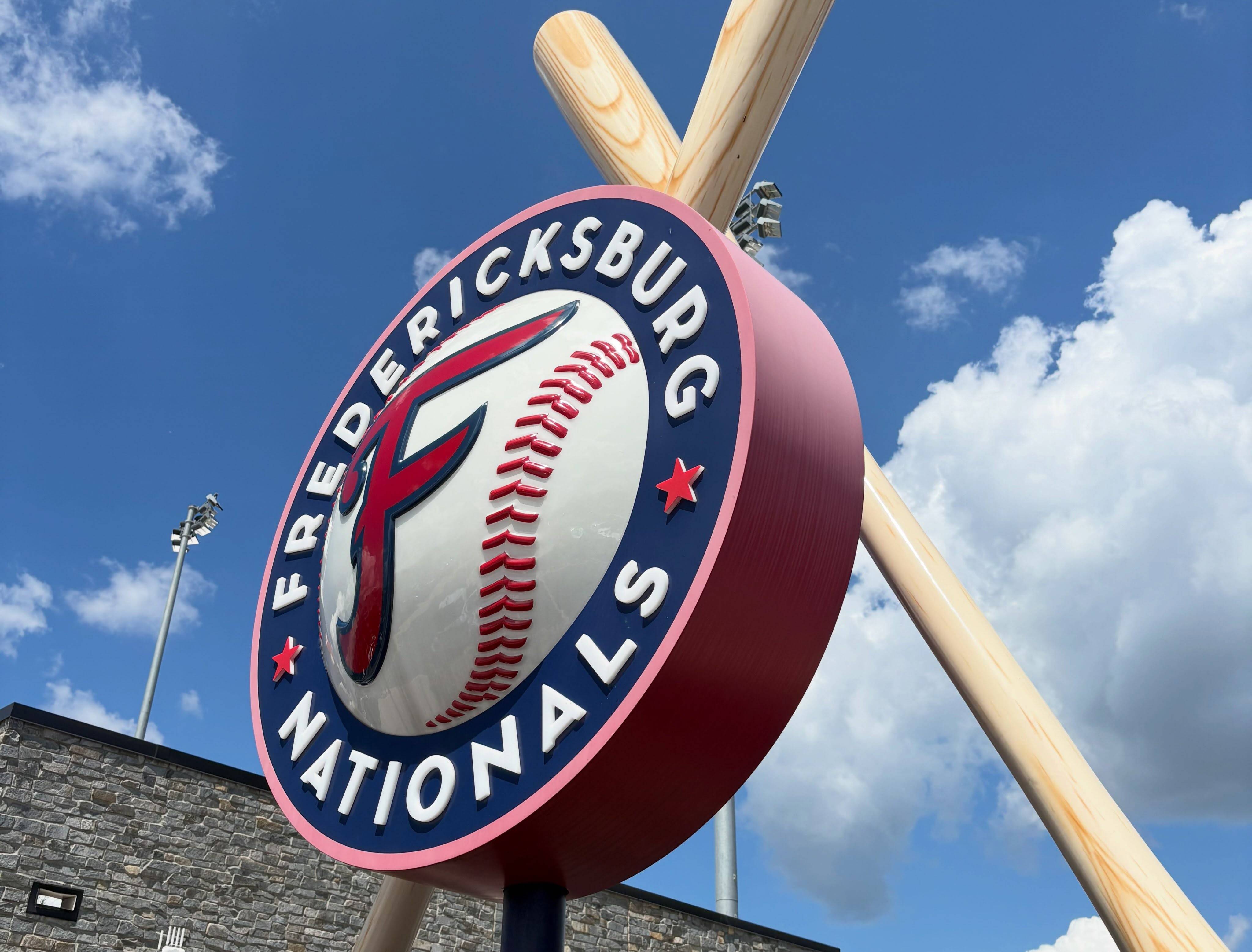 The Fredericksburg Nationals logo sign, a baseball-and-F emblem between two crossed bats, against a blue sky.