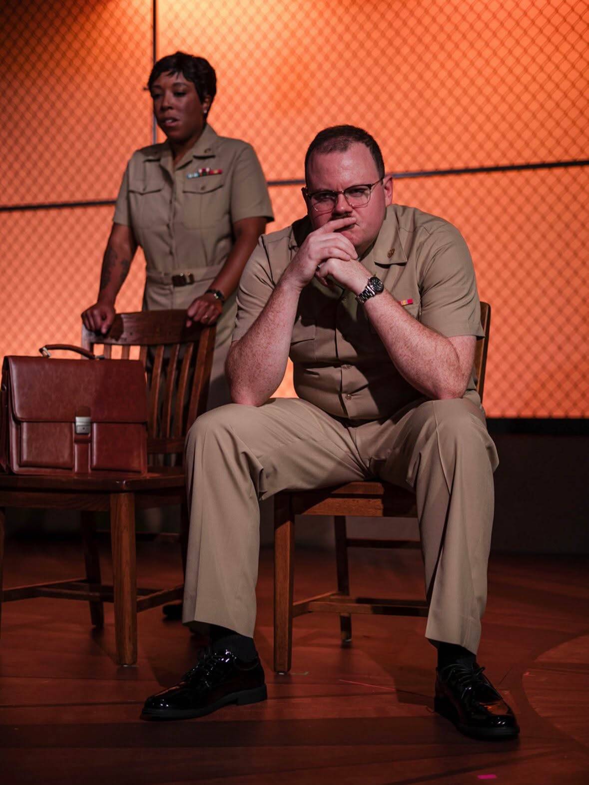 Two uniformed performers appear together, with one standing behind the other.