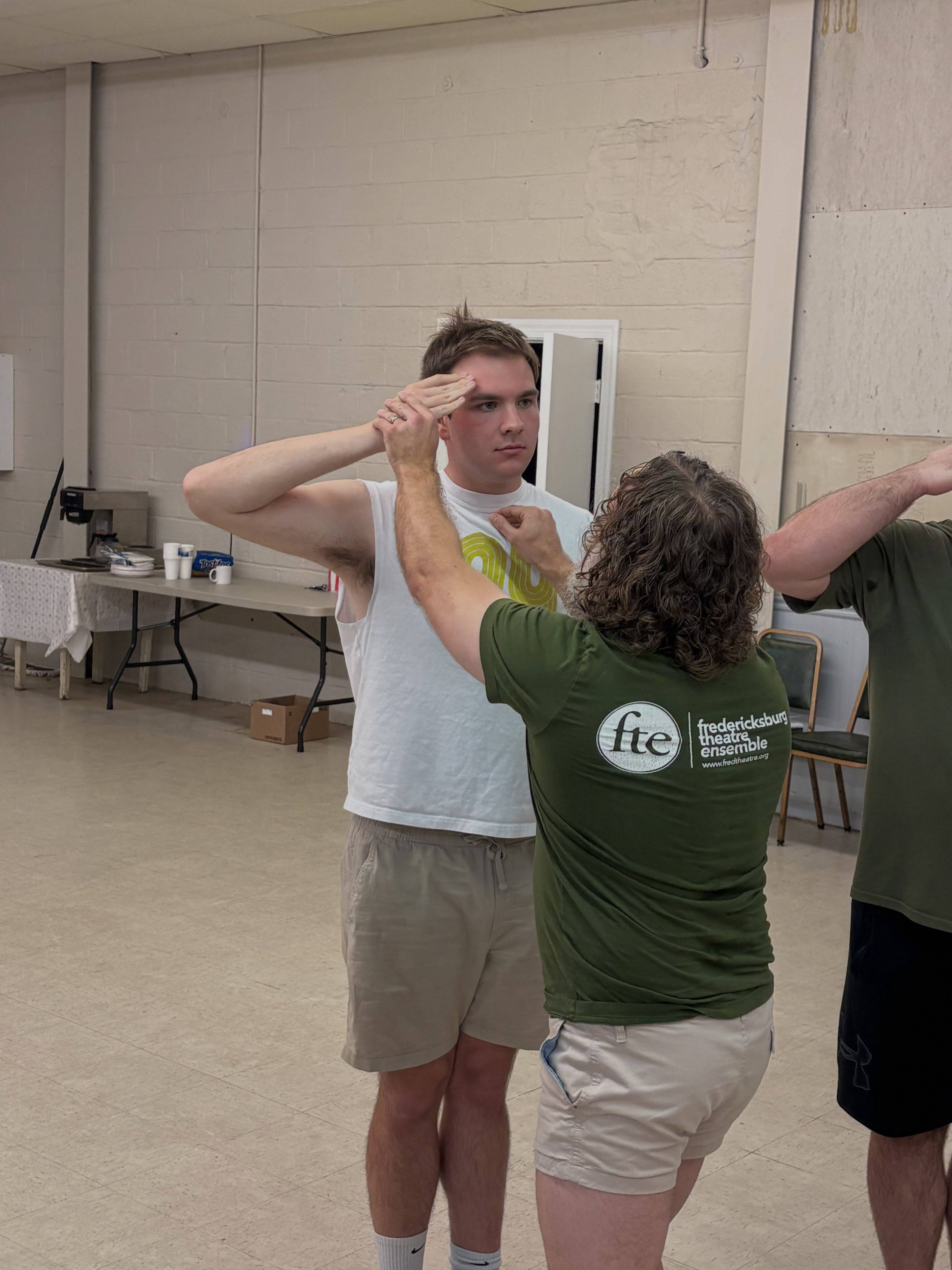 Assistant Director Doy Demsick adjusts a cast member’s hand into a correct salute during rehearsal.