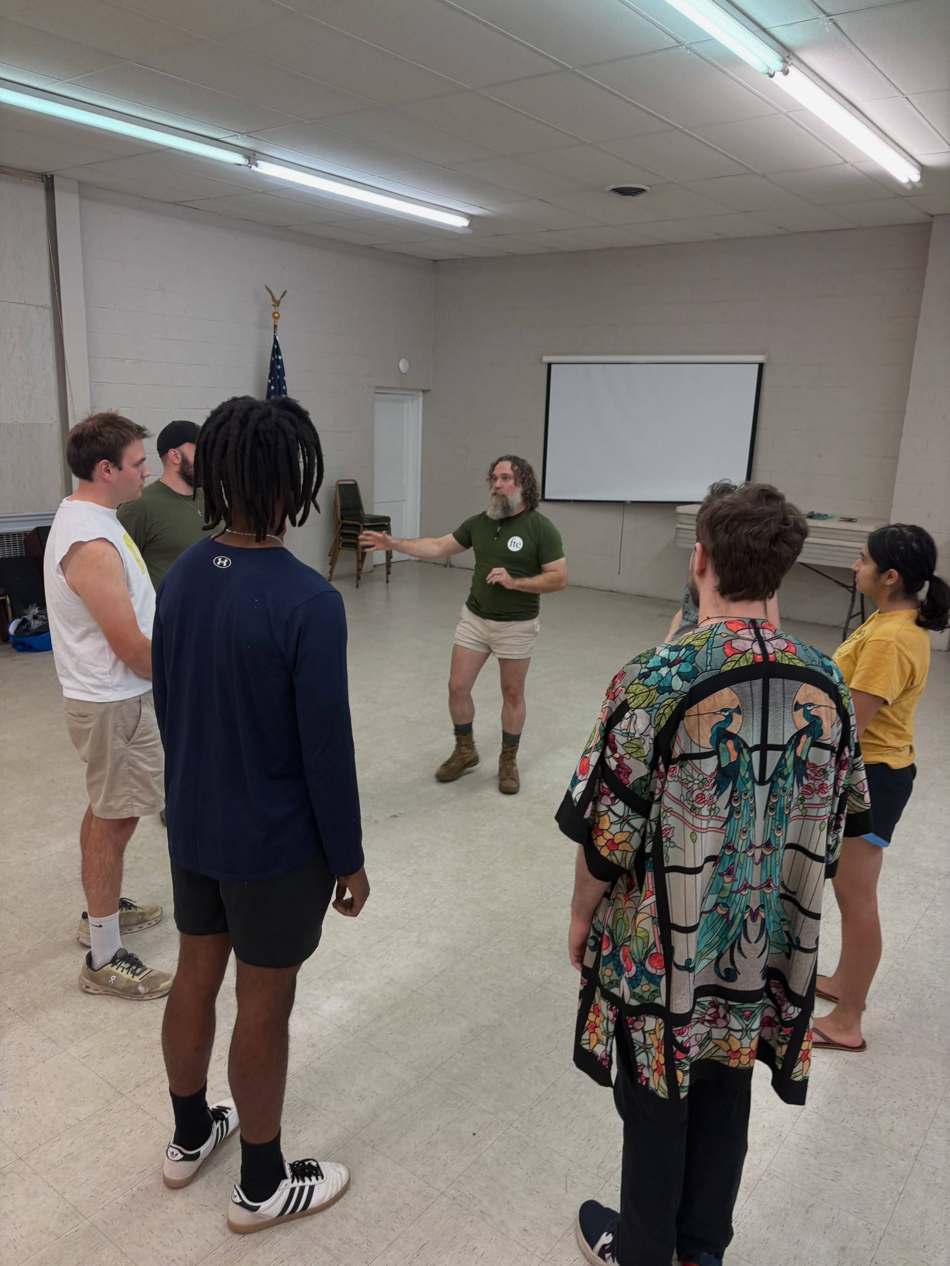 Doy Demsick addresses the cast gathered in a loose circle in the rehearsal hall.