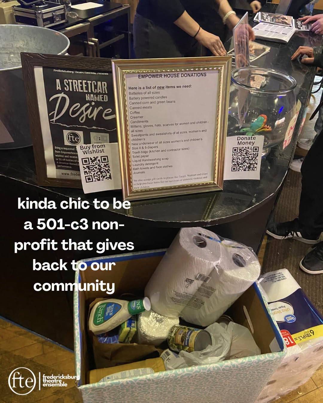 A lobby table of collected Empower House donations beside a Streetcar Named Desire poster, captioned kinda chic to be a 501-c3 non-profit that gives back to our community.
