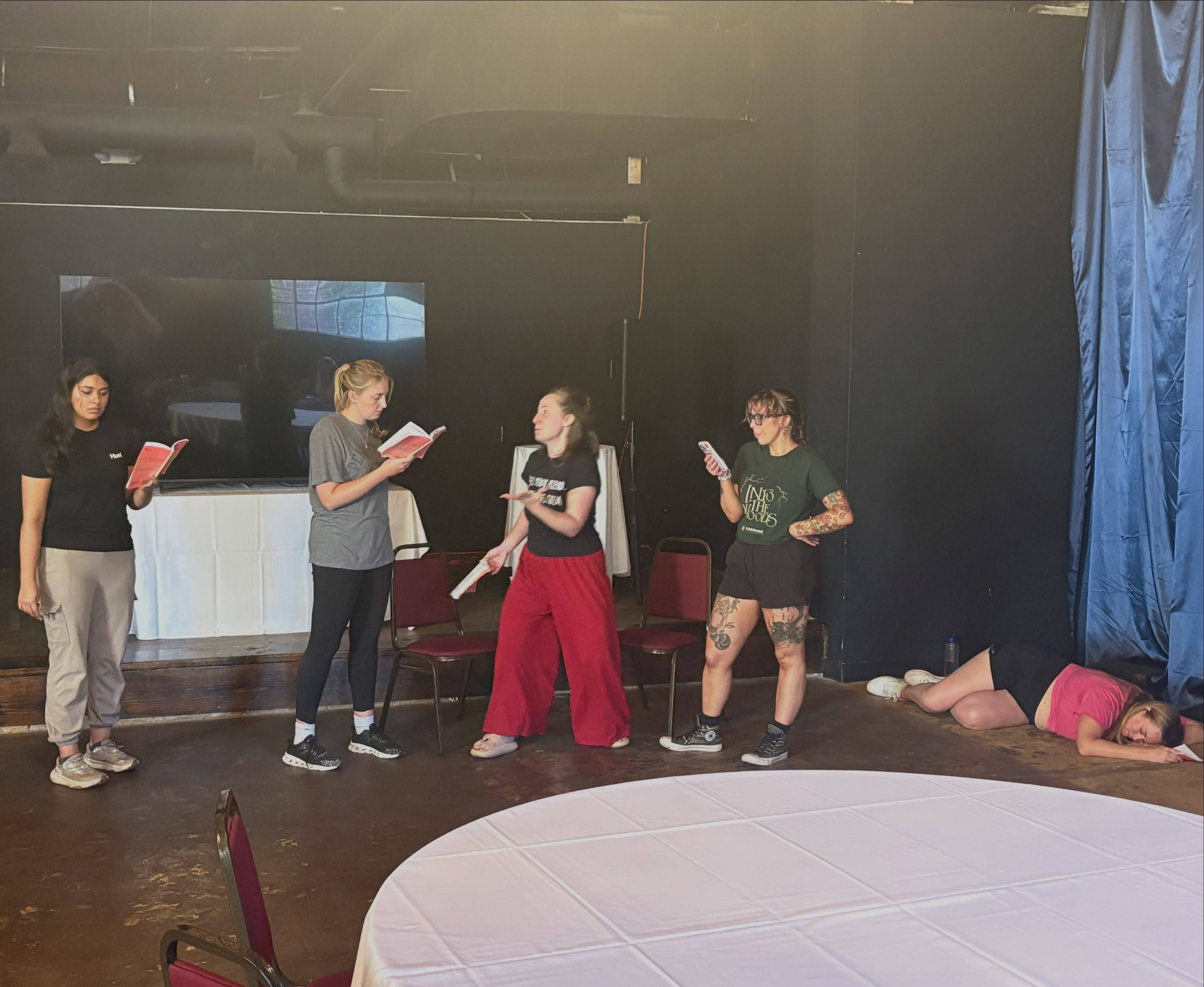 Five performers rehearse on stage, with one performer lying on the floor.