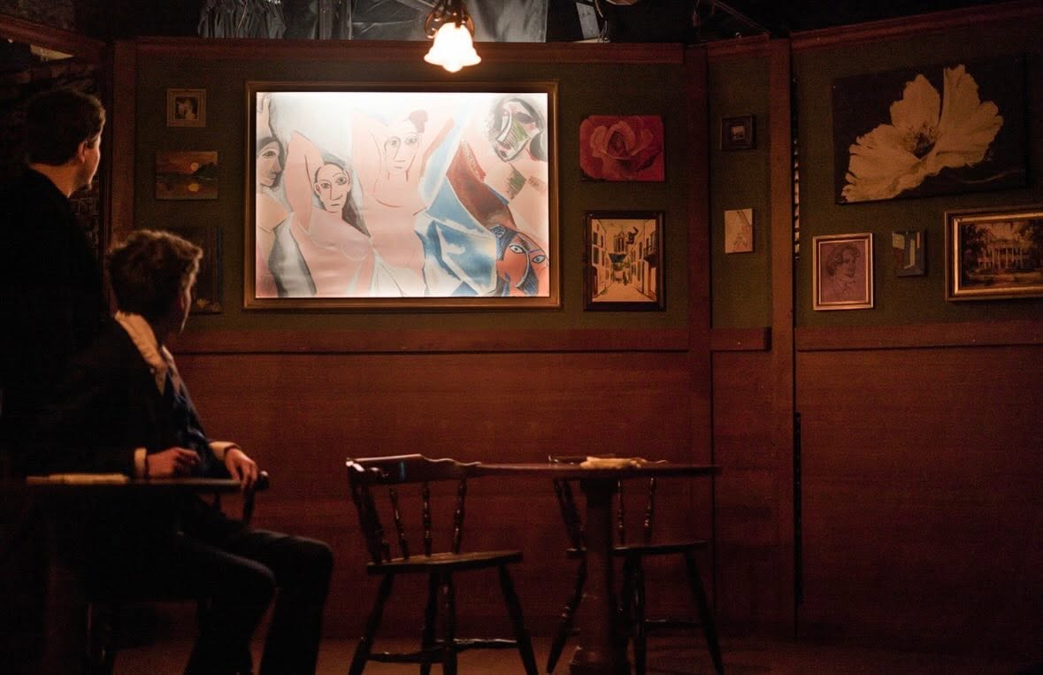 Two audience members in the dim Lapin Agile bar set gaze at a glowing painting in the style of Picasso's Les Demoiselles d'Avignon.